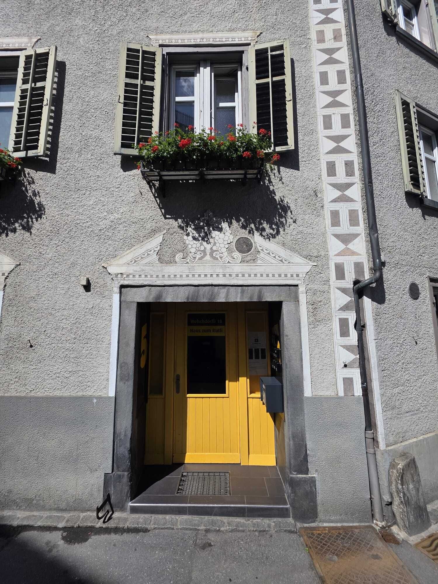 A building with a yellow door, a sign above the door, and a flower box with red flowers.