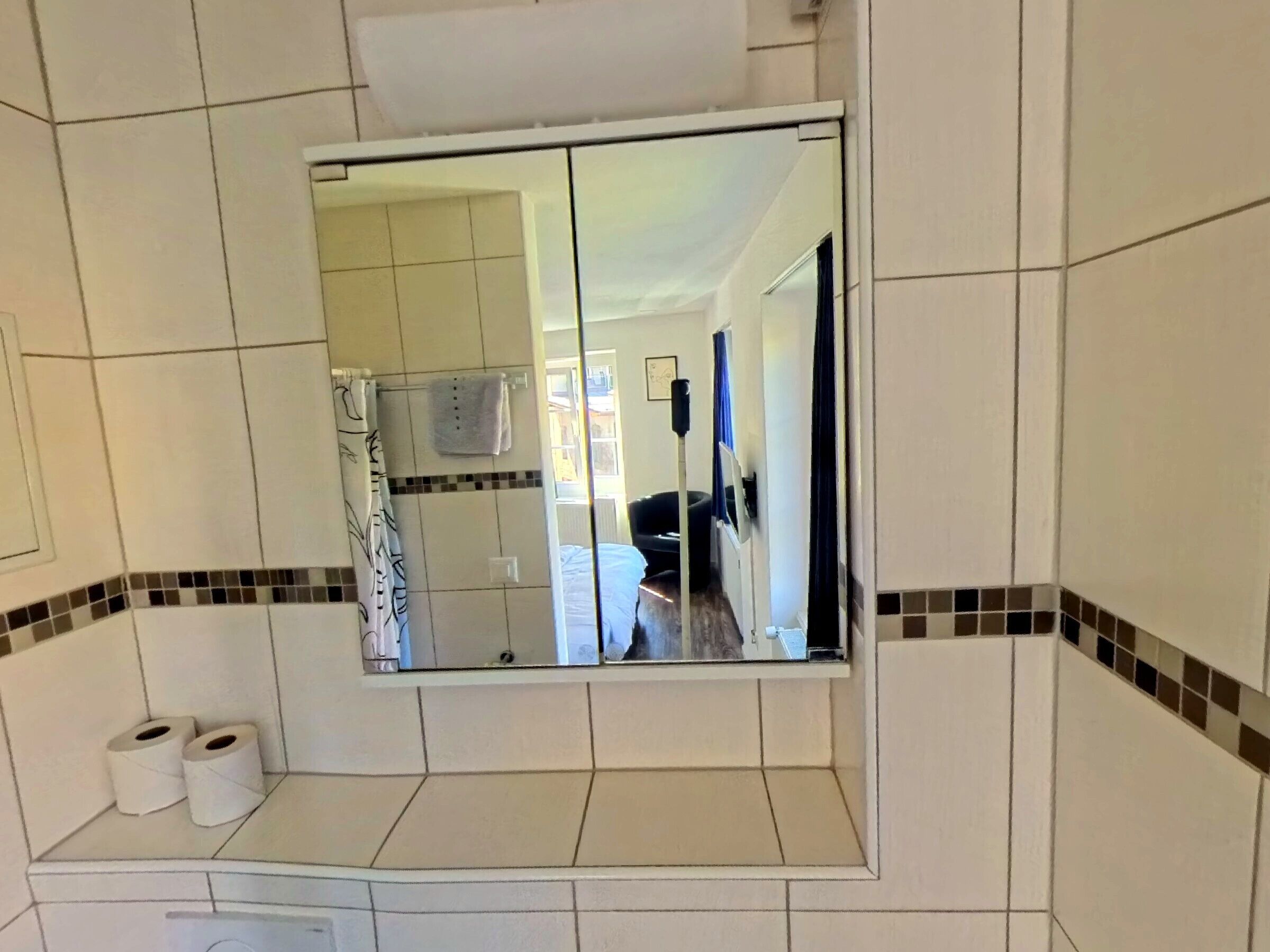 A bathroom with a mirror, a towel rack, and two rolls of toilet paper.