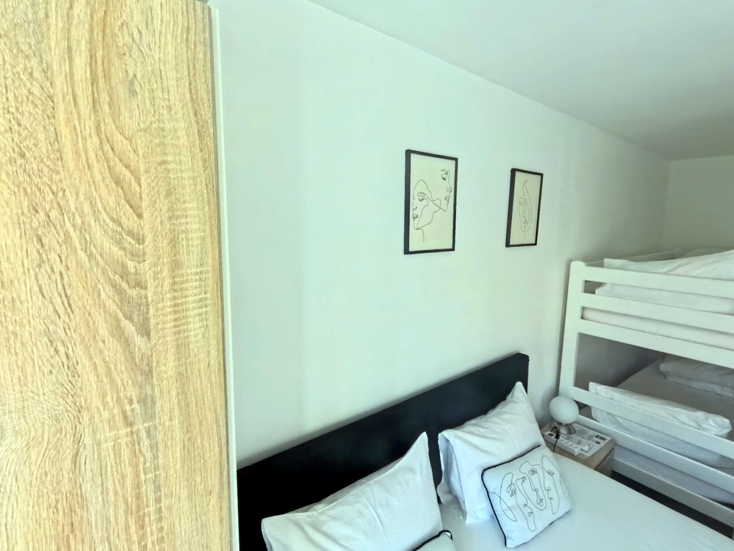 A bedroom with a bunk bed, white bedding, and two framed artworks on the wall.