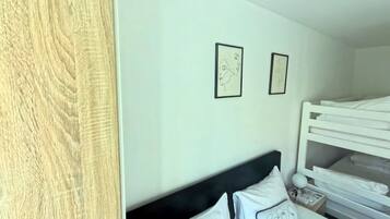A bedroom with a bunk bed, white bedding, and two framed artworks on the wall.