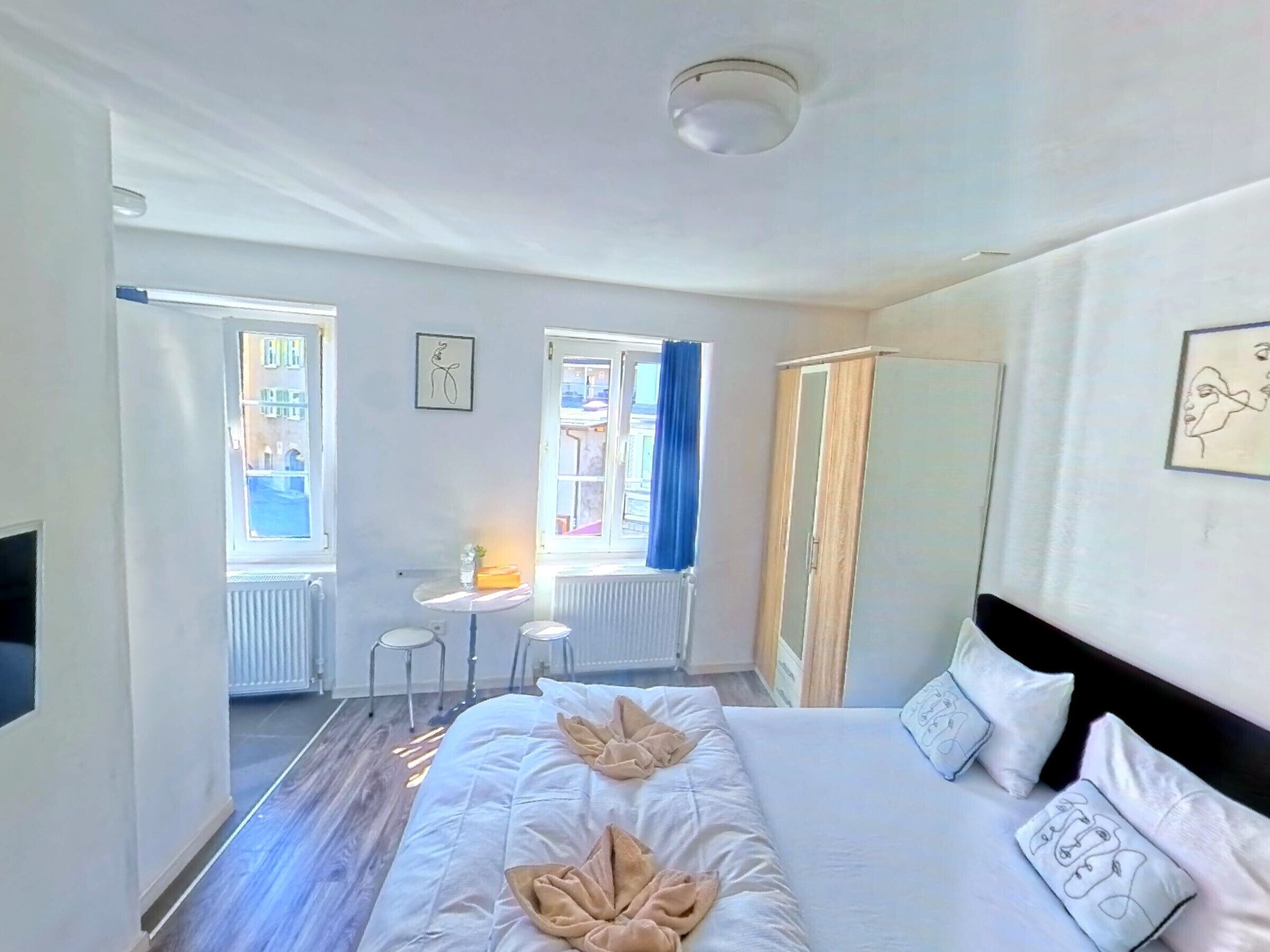 A hotel room with a large bed, a desk, two chairs, a radiator, and a window with curtains.