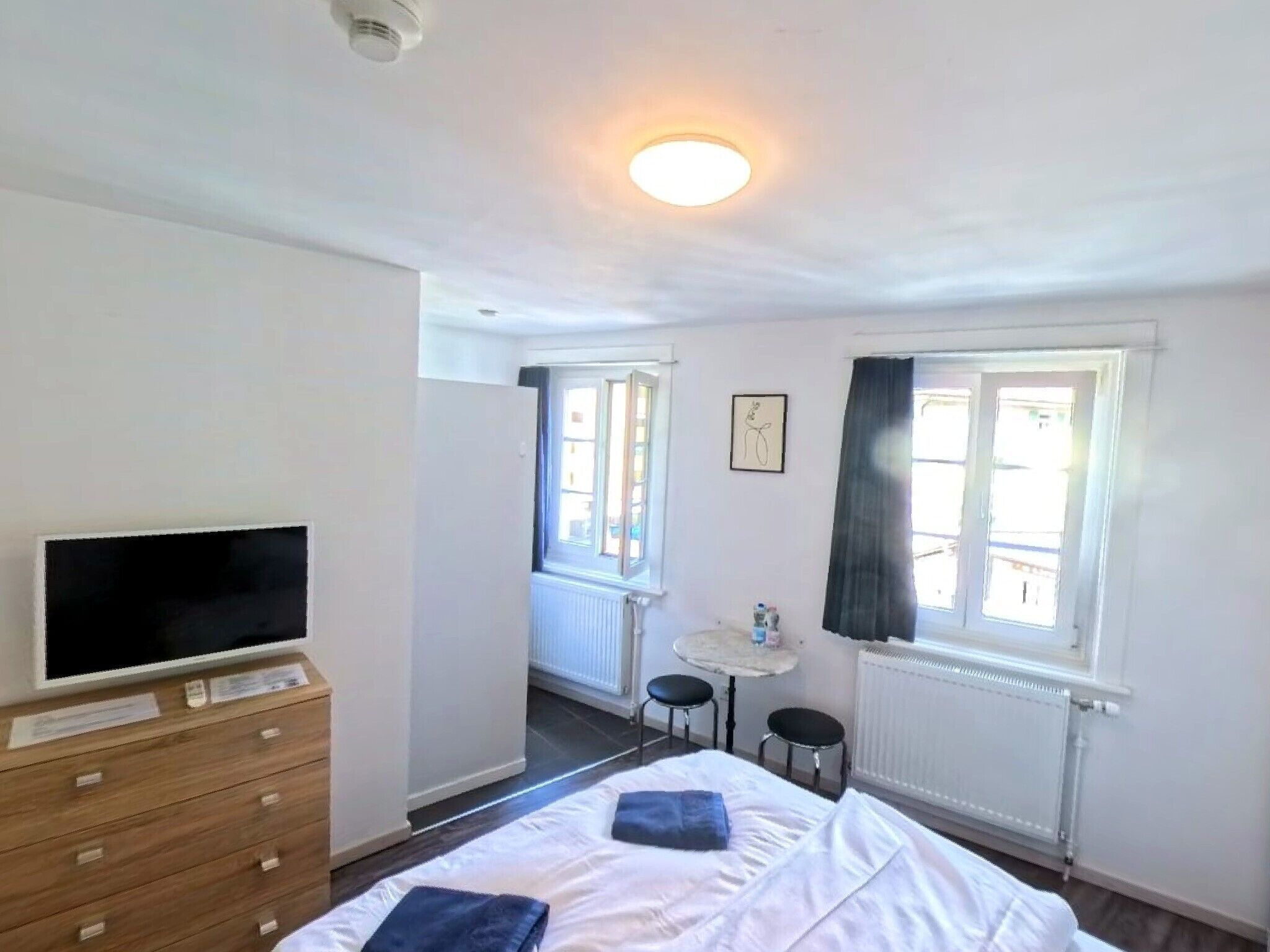 A hotel room with a bed, a TV, a dresser, a small table, and a window with curtains.