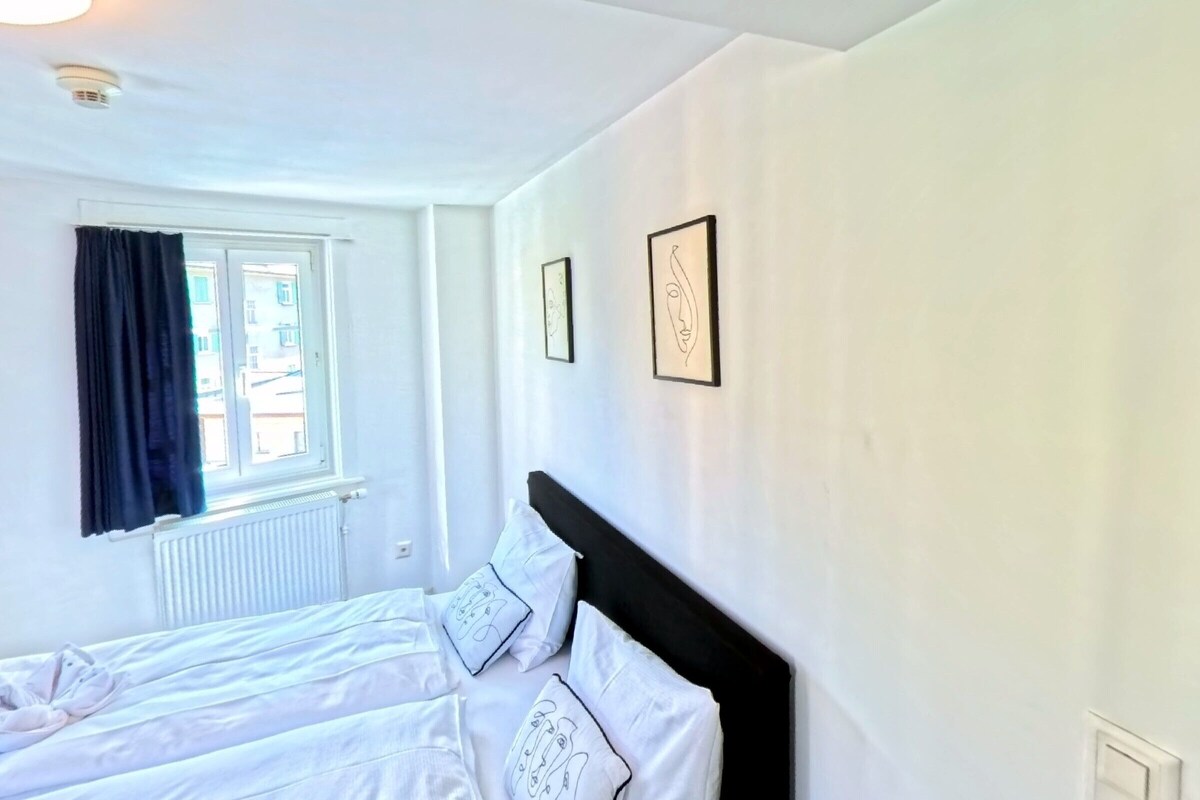A hotel room with a bed, a window with curtains, and a wall-mounted picture.