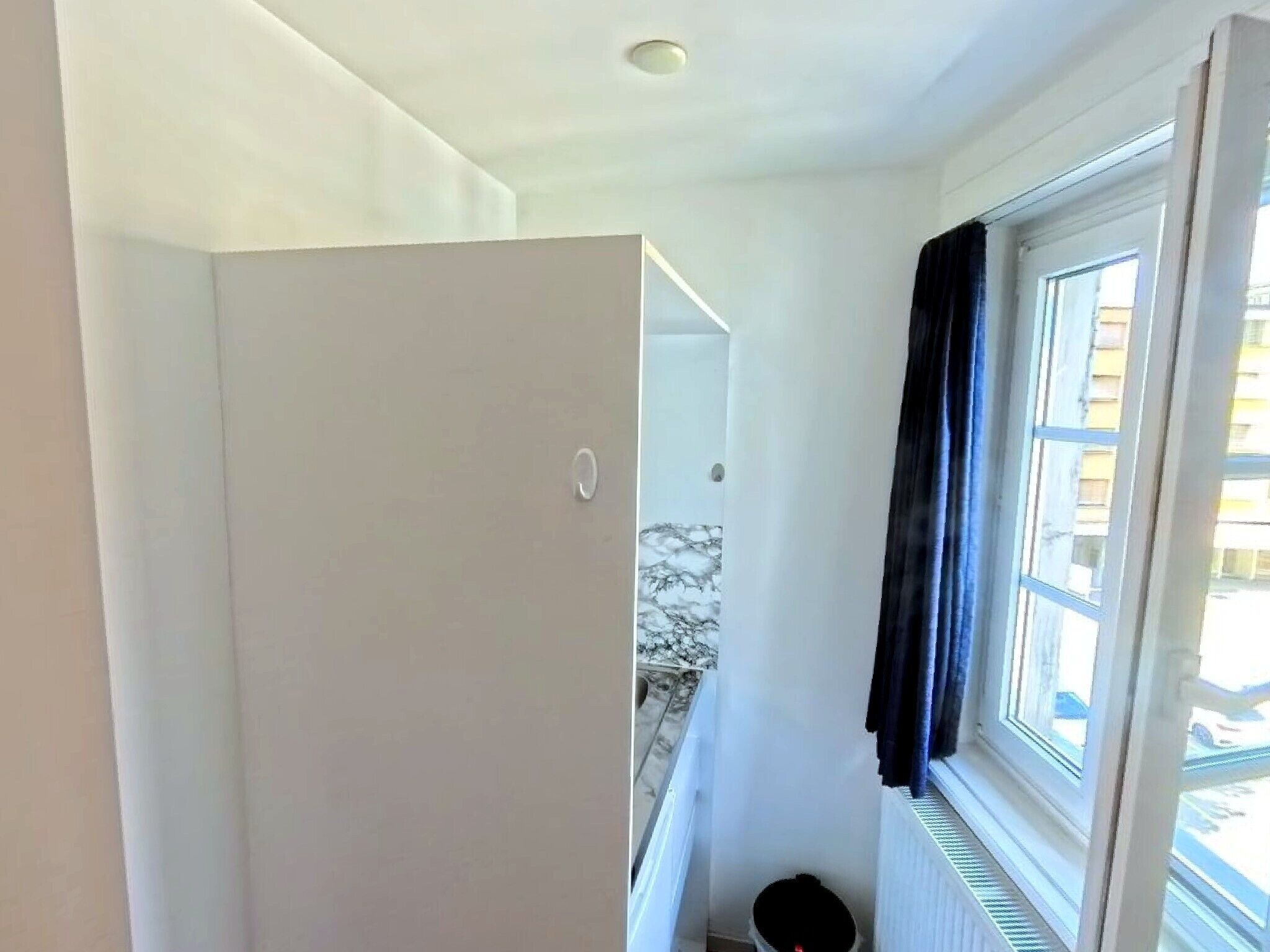 Ein Zimmer mit einem weißen Kleiderschrank, einem Heizkörper und einem fenster mit Vorhängen.