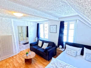 Habitación de hotel moderna con sofá, cama, una mesita redonda y zona de ducha.