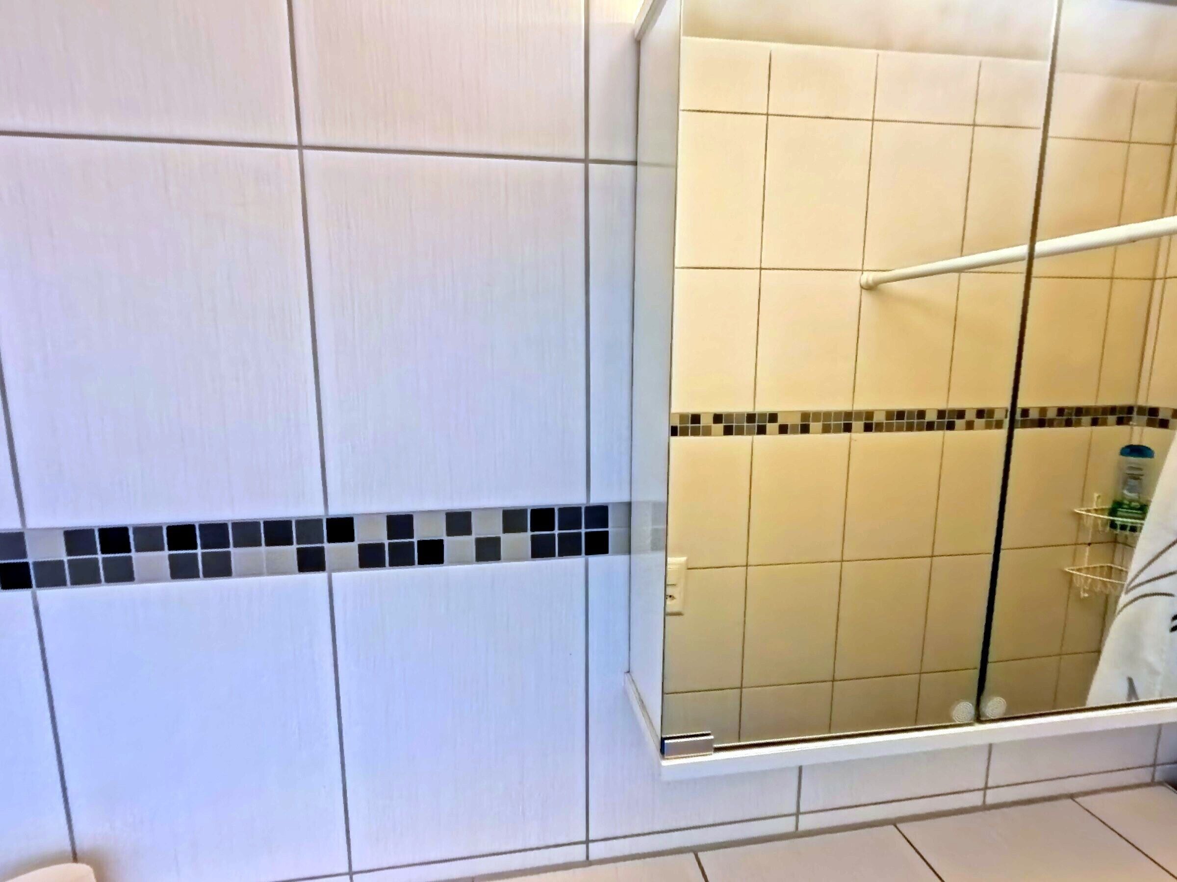 A bathroom with white tiles, a glass shower enclosure, and a tiled border.