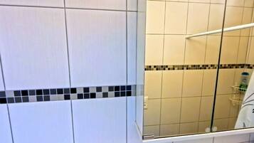 A bathroom with white tiles, a glass shower enclosure, and a tiled border.