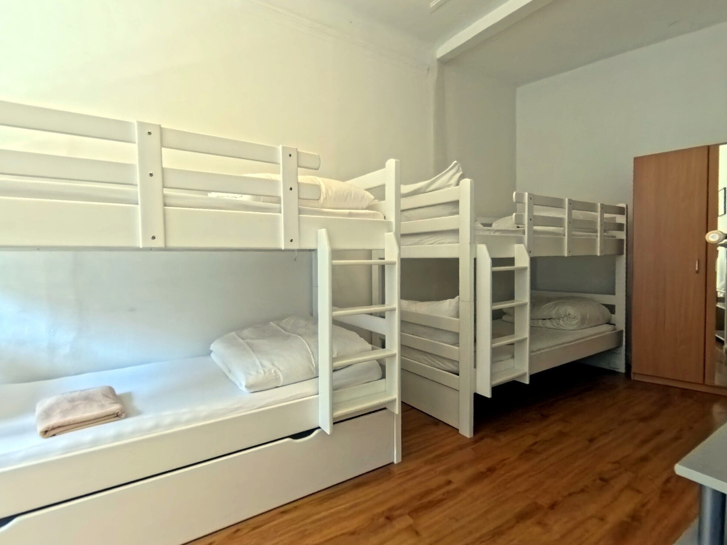 A room with bunk beds, wooden flooring, and a wooden wardrobe.
