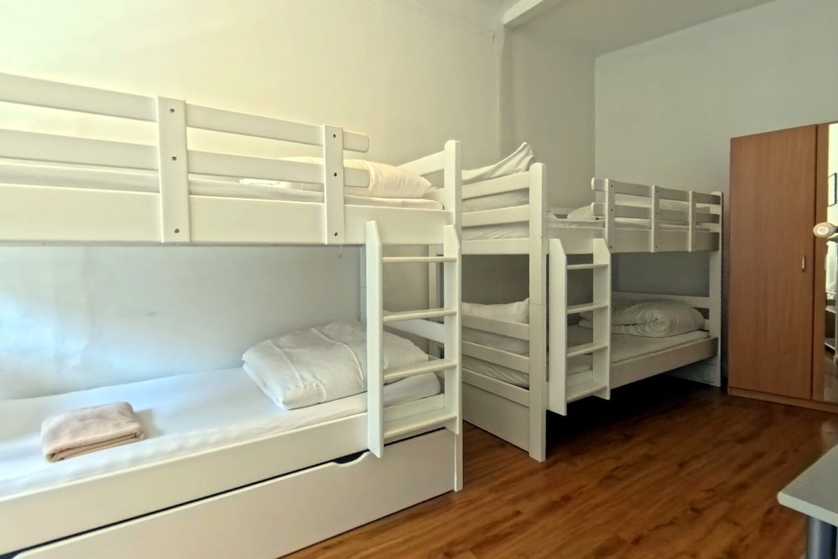 A room with bunk beds, wooden flooring, and a wooden wardrobe.