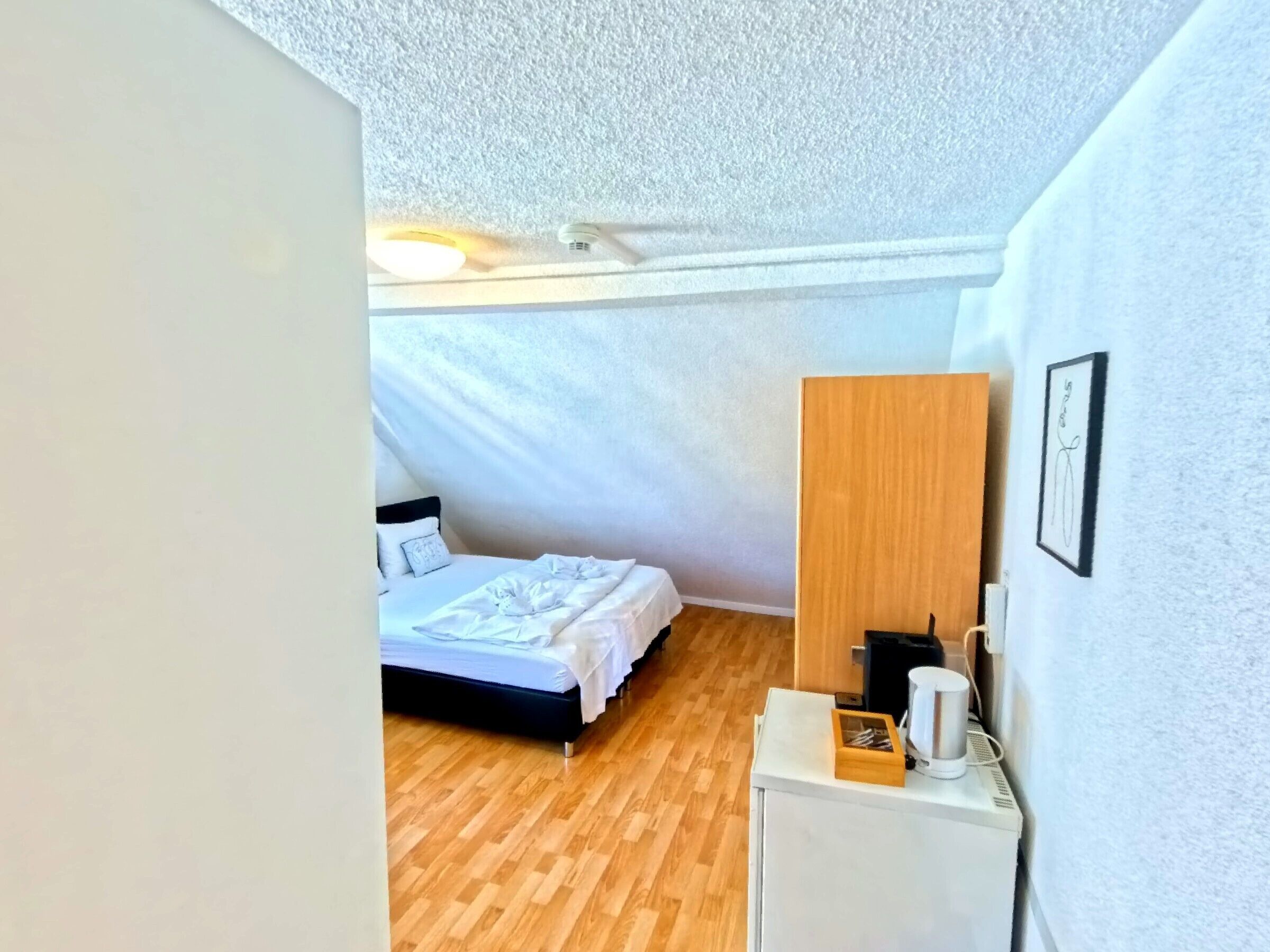Un dormitorio con una cama, un aparador de madera y una pared blanca con un cuadro enmarcado.