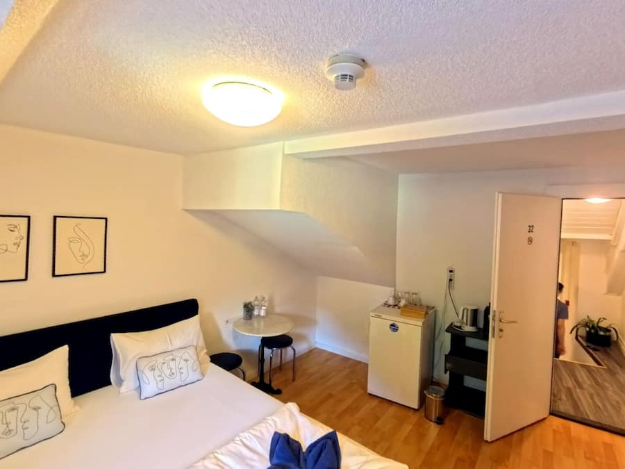 Une chambre d’hôtel avec un lit, un bureau, un petit réfrigérateur et une porte donnant sur une autre pièce.