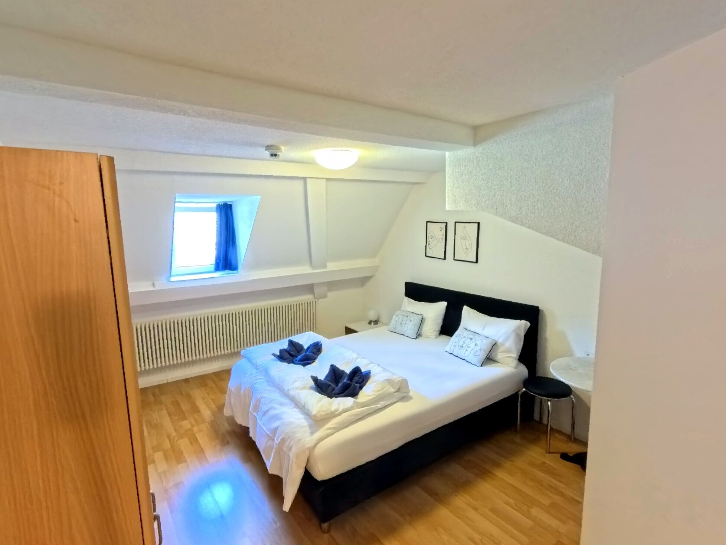 Quarto com cama, janela, radiador e uma pequena mesa.