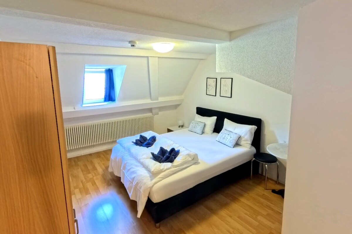 A bedroom with a bed, a window, a radiator, and a small table.