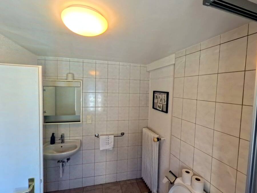 Une salle de bain avec des carreaux blancs, un lavabo, un miroir, un porte-serviettes et un radiateur.