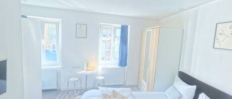 A hotel room with a large bed, a bedside table, a chair, and a window with curtains.