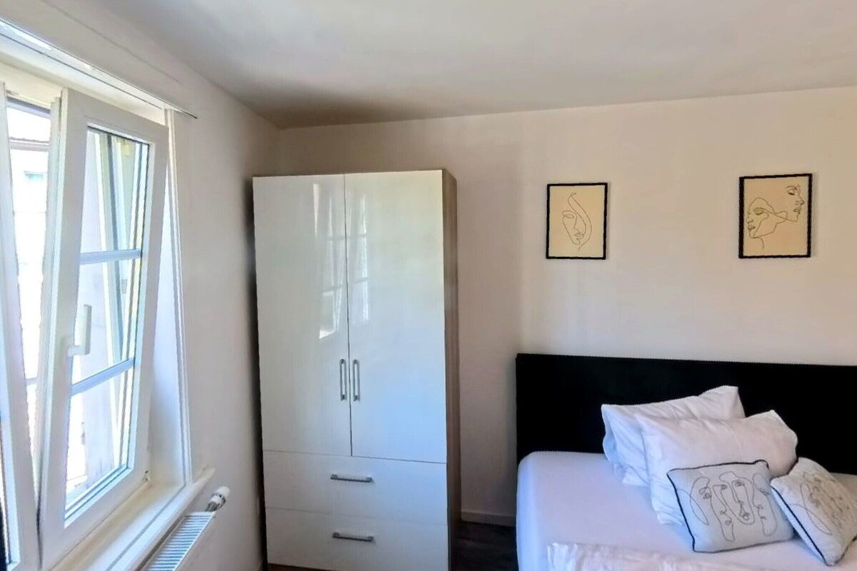 A bedroom with a bed, a wardrobe, and two wall-mounted artworks.