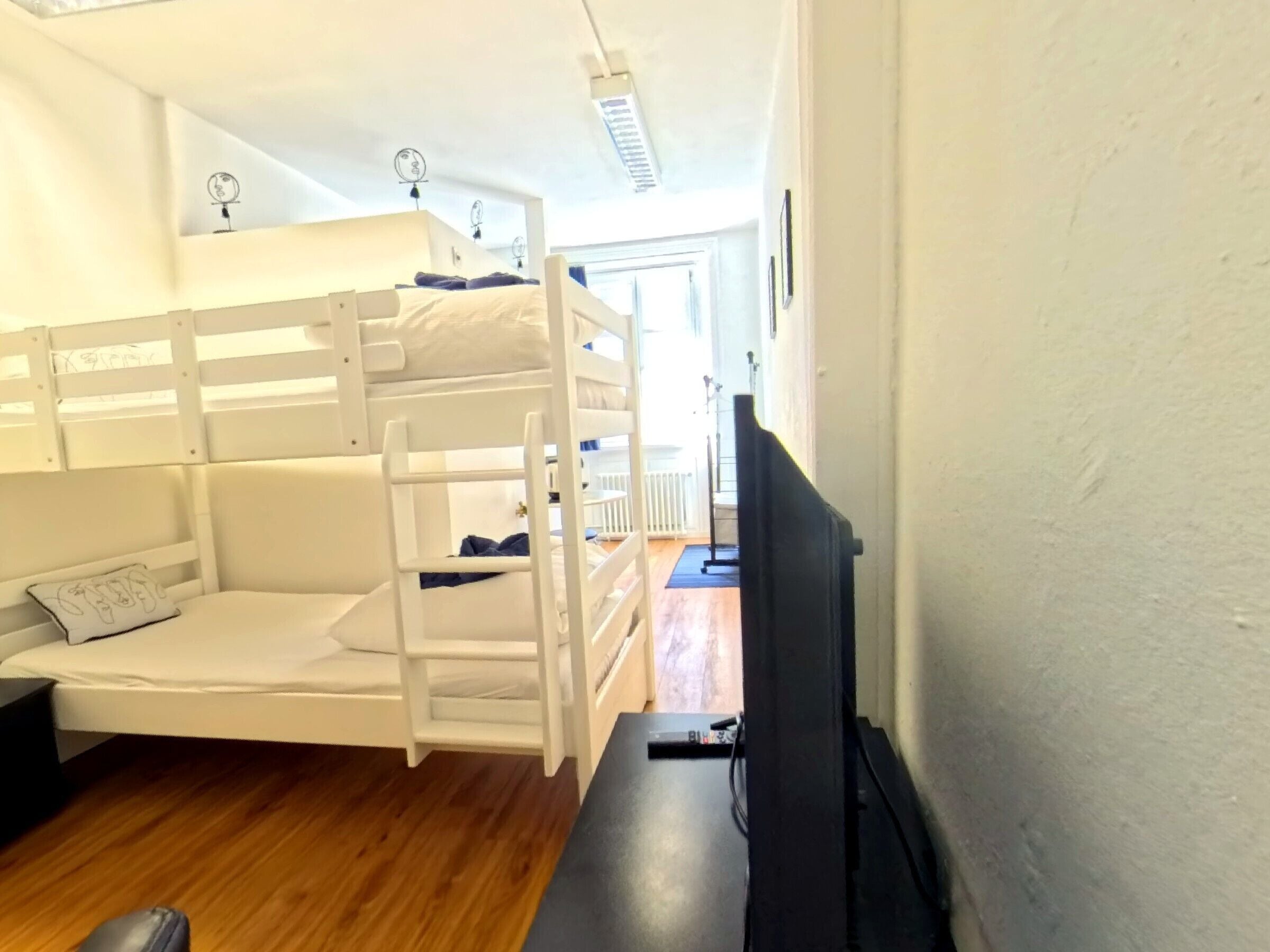 A bunk bed room with a television on a stand, wooden flooring, and a door leading to another room.