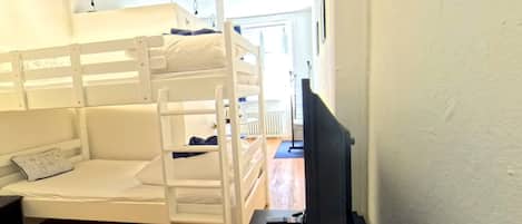 A bunk bed room with a television on a stand, wooden flooring, and a door leading to another room.