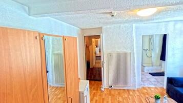 Une chambre avec une armoire en bois, un radiateur, une cabine de douche en verre et une petite table sur laquelle se trouvent une plante et une bouteille.