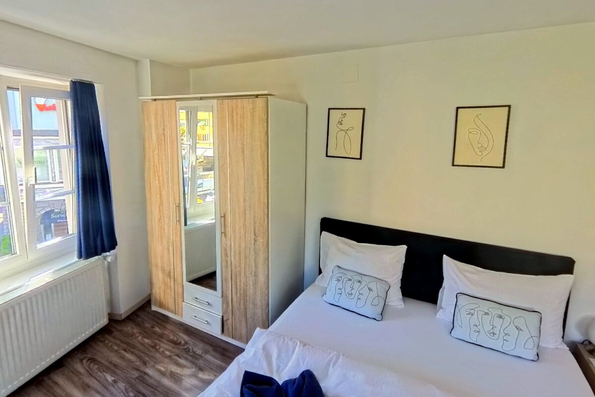 A bedroom with a bed, a wardrobe, and two framed artworks on the wall.
