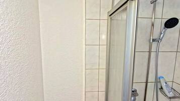 Ein Duschbereich mit Glastür, Handbrause und am Wand montierter Armatur.