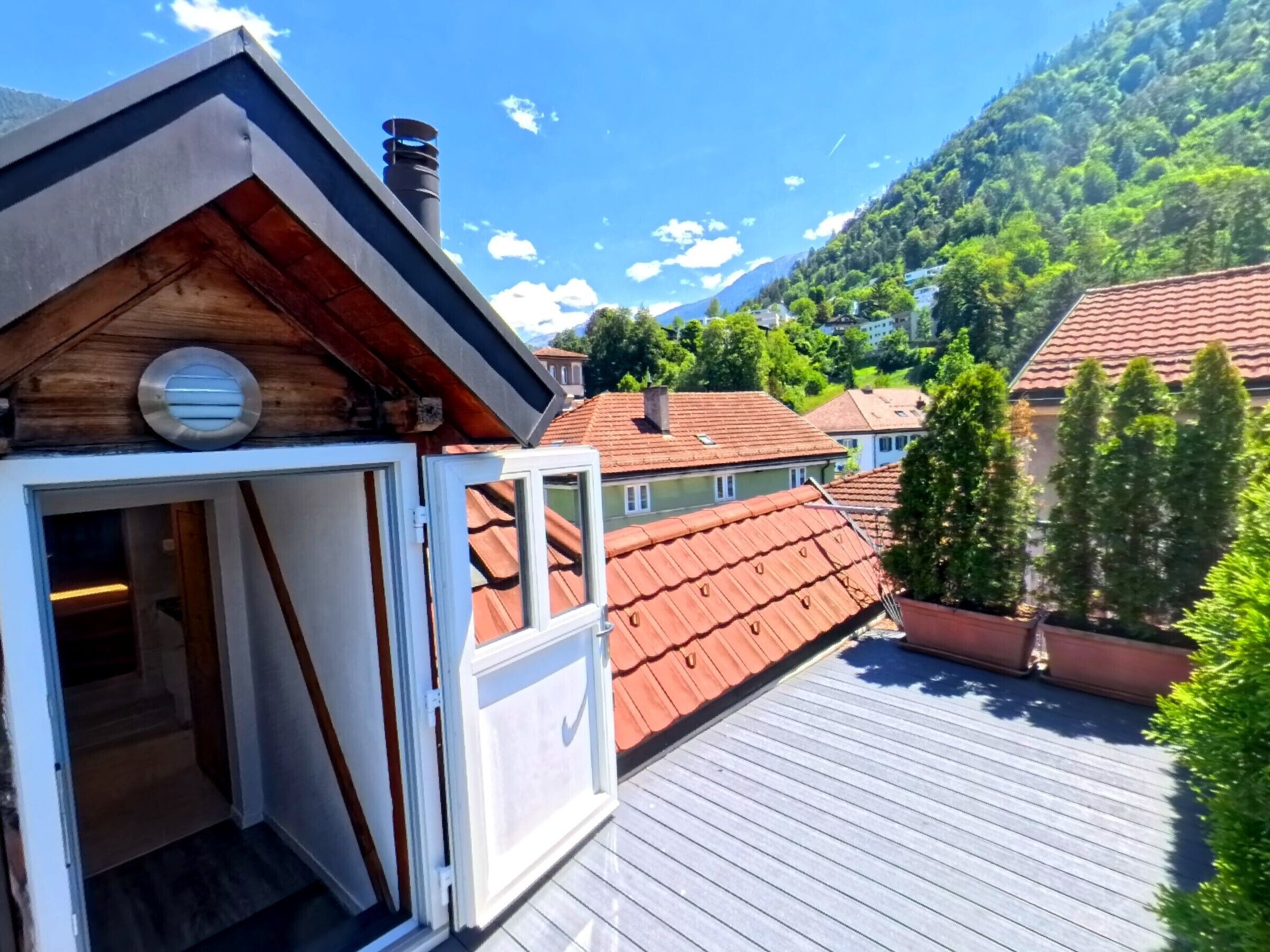 Une terrasse en bois offrant une vue sur une montagne et les maisons voisines.