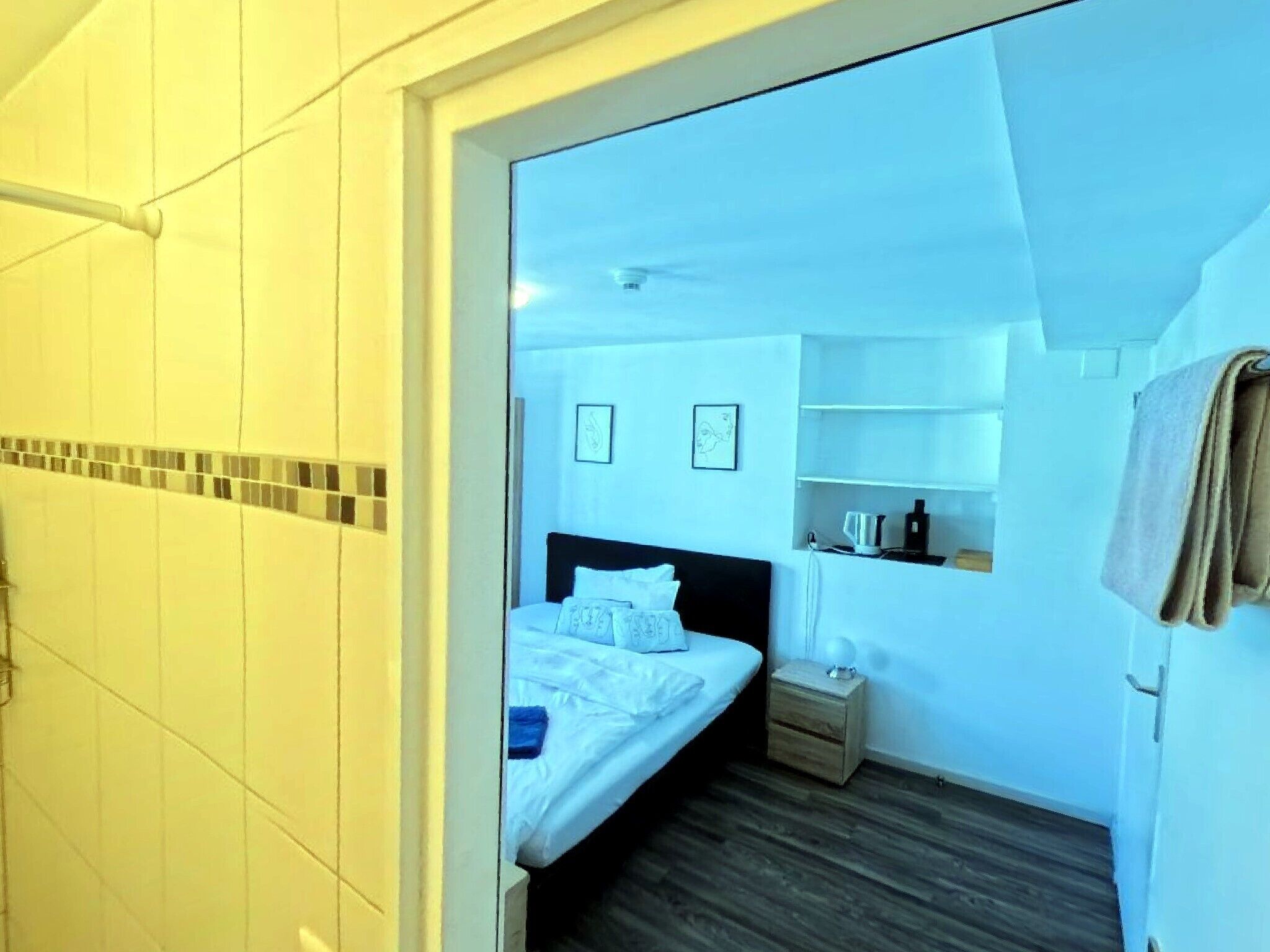 A hotel room with a bed, bedside table, and a small shelf with toiletries.