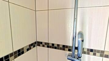 Un espace douche doté d’une pomme de douche chromée et d’un mur carrelé.
