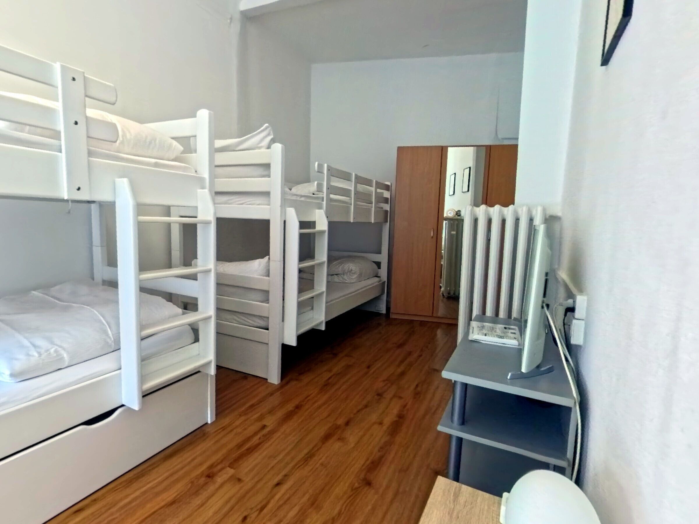 Een slaapzaal met stapelbedden, een houten vloer, een radiator en een bureau met stoel.