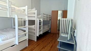 Een slaapzaal met stapelbedden, een houten vloer, een radiator en een bureau met stoel.