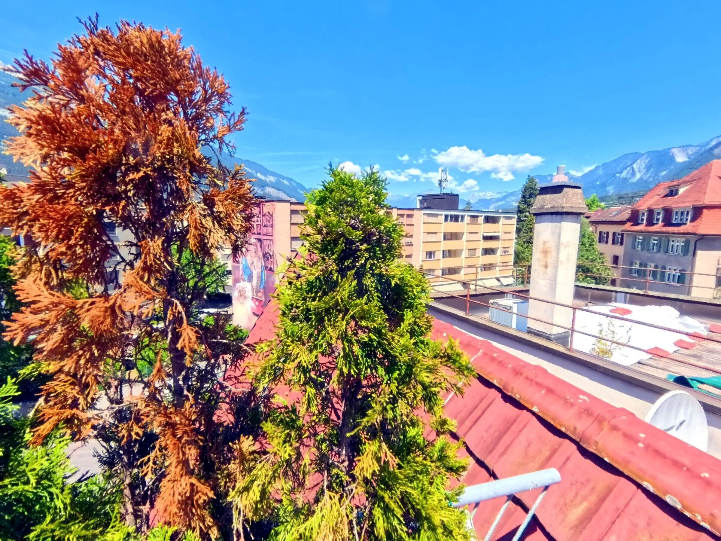 A rooftop with a view of mountains, buildings, and trees.