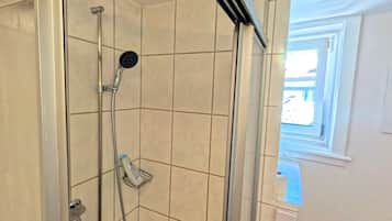 Een douche met een handdouche, een zeepdispenser en een raam met uitzicht.