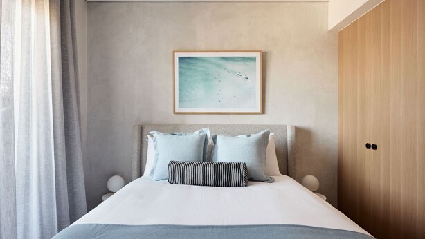 Une chambre à coucher avec un lit, des oreillers, un tableau encadré et une armoire en bois.