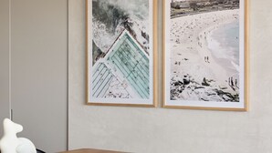Deux tableaux encadrés sont accrochés au mur : l’un représente une scène de plage et l’autre, un bâtiment avec un toit bleu.