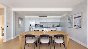 Une cuisine moderne avec des meubles blancs, un îlot central et un coin repas comprenant une table en bois et quatre chaises.