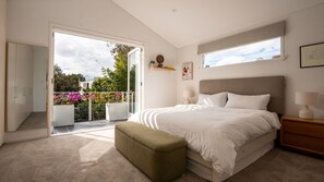 A bedroom with a large bed, a nightstand, a bench, a sliding glass door to a balcony, and a view of the outdoors. - Alora House, North Bondi (North Bondi)
