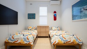 Een slaapkamer met twee bedden, een dressoir, een aan de muur bevestigde televisie, een schilderij en een raam met jaloezieën.