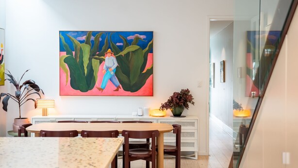 Een eethoek met een tafel, stoelen, een schilderij aan de muur en een plant aan de zijkant.