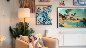 Een woonkamer met een bank, een lamp en een schilderij van een tropisch resort.