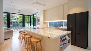 Une cuisine moderne dotée d’un grand îlot central, de tabourets de bar, d’un réfrigérateur noir et offrant une vue sur l’espace extérieur.