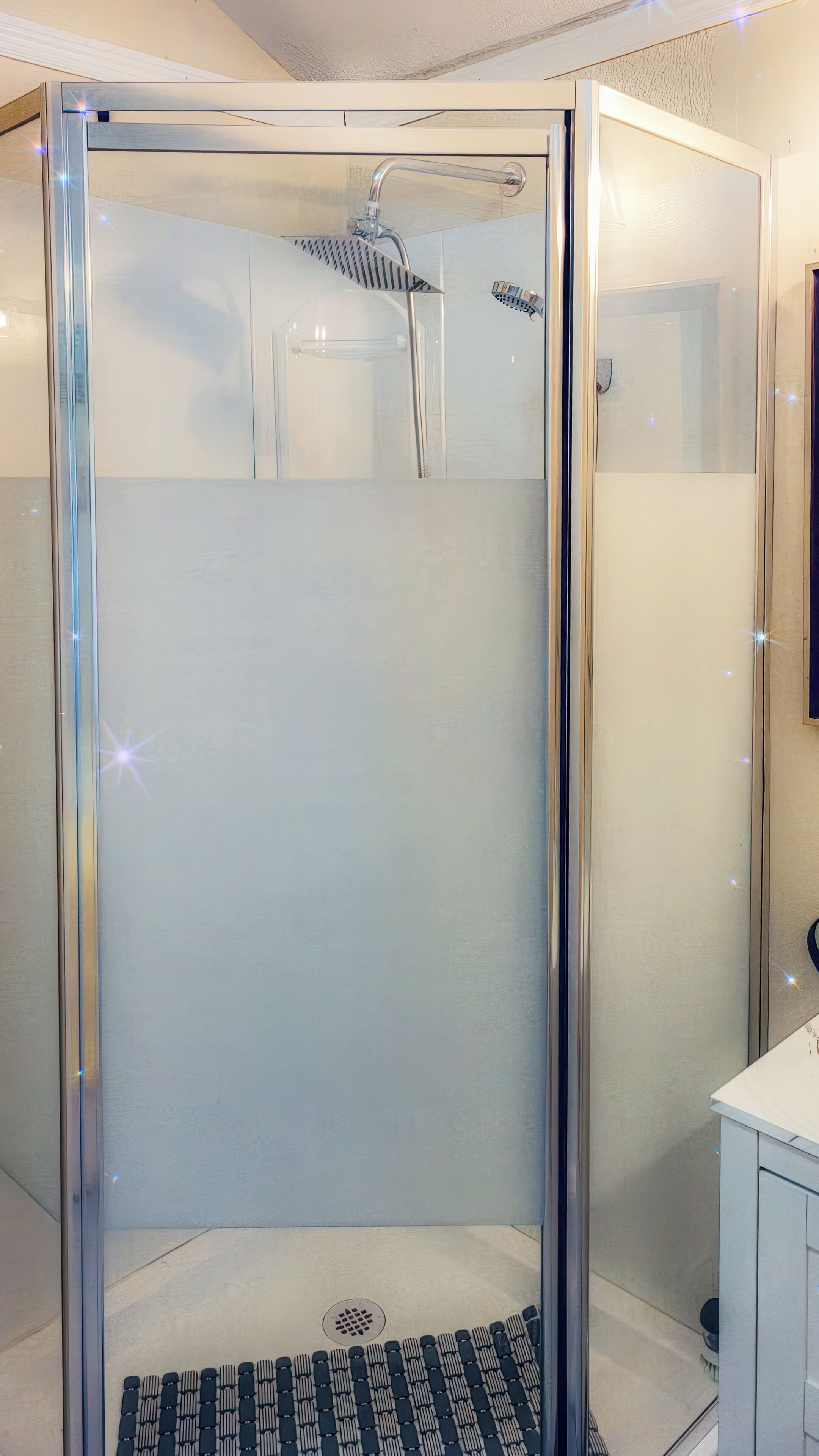 Cabina de ducha con paredes de vidrio, ducha de mano y desagüe.