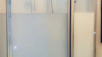 Cabina de ducha con paredes de vidrio, ducha de mano y desagüe.
