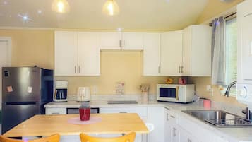 Una cocina compacta con armarios blancos, un refrigerador, una cafetera, un microondas y un lavaplatos.