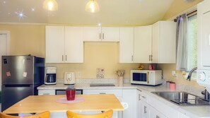 A compact kitchen with white cabinets, a refrigerator, a coffee maker, a microwave, and a sink. - The Blue Sunshine Retreat (Citra)