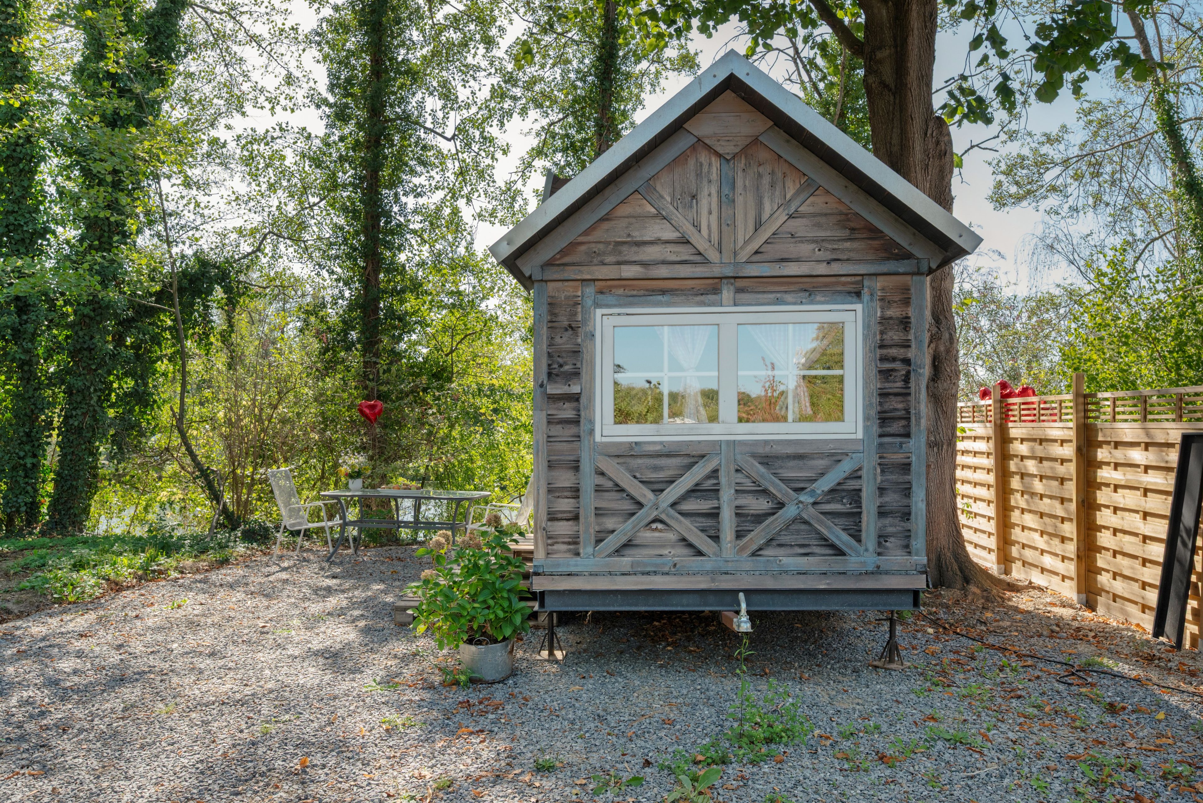 Eine kleine Holzhütte mit Fenster, umgeben von Bäumen und einem Kiesweg.