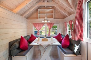 Ein gemütliches Blockhaus-Interieur mit Holzvertäfelung, einem zentralen Tisch mit Kerzen und karierten Vorhängen.