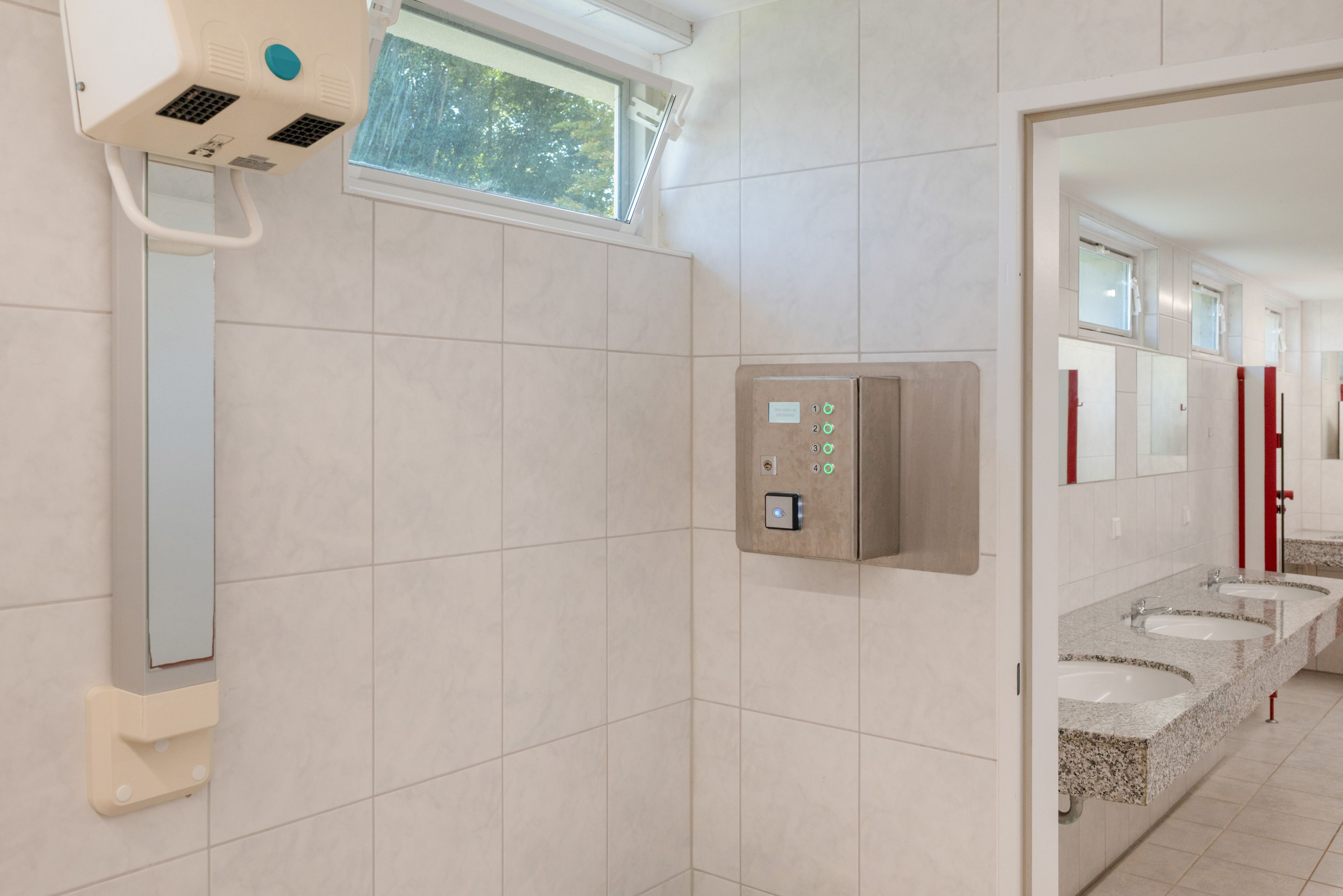 Un baño moderno con un secador de manos, un panel de control y una ventana.