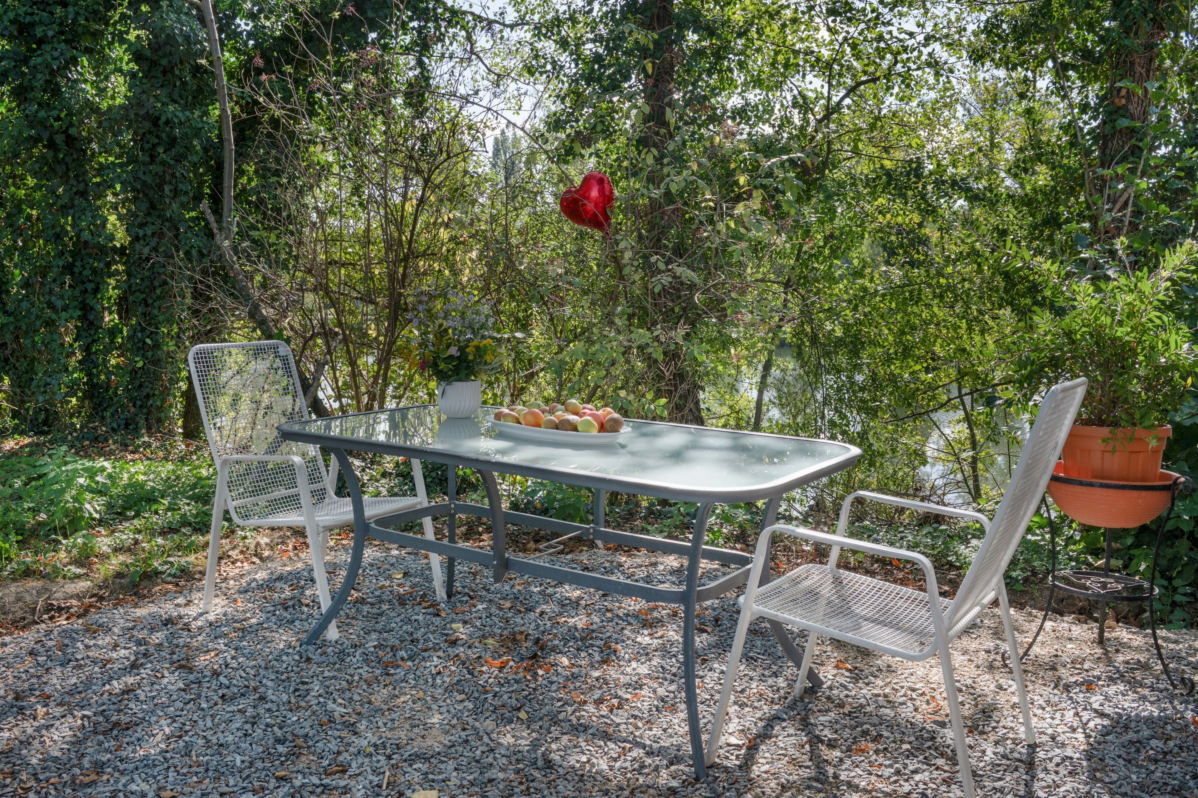An outdoor dining area with a table and chairs, surrounded by greenery.