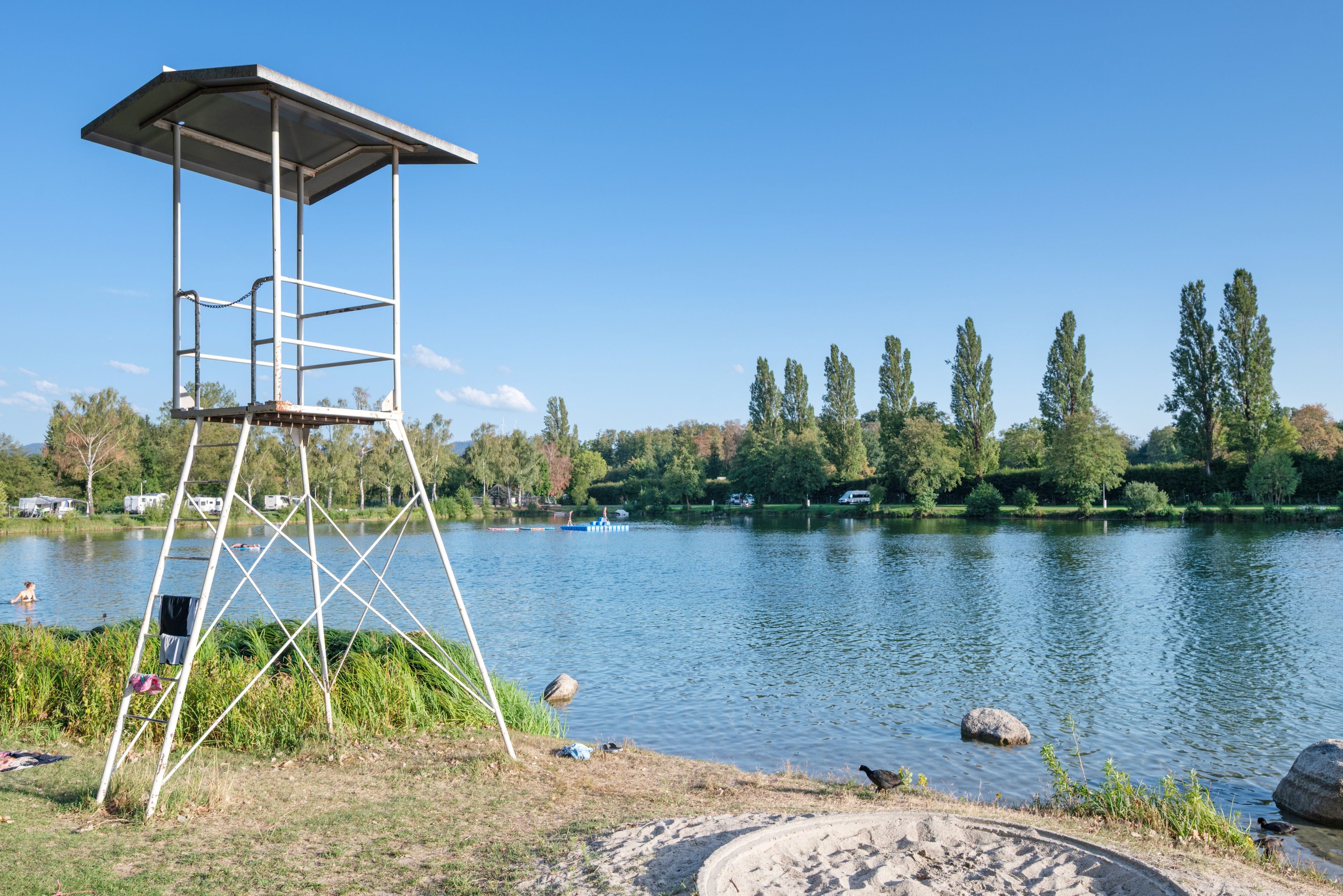 Ein Rettungsturm an einem See bei blauem Himmel.