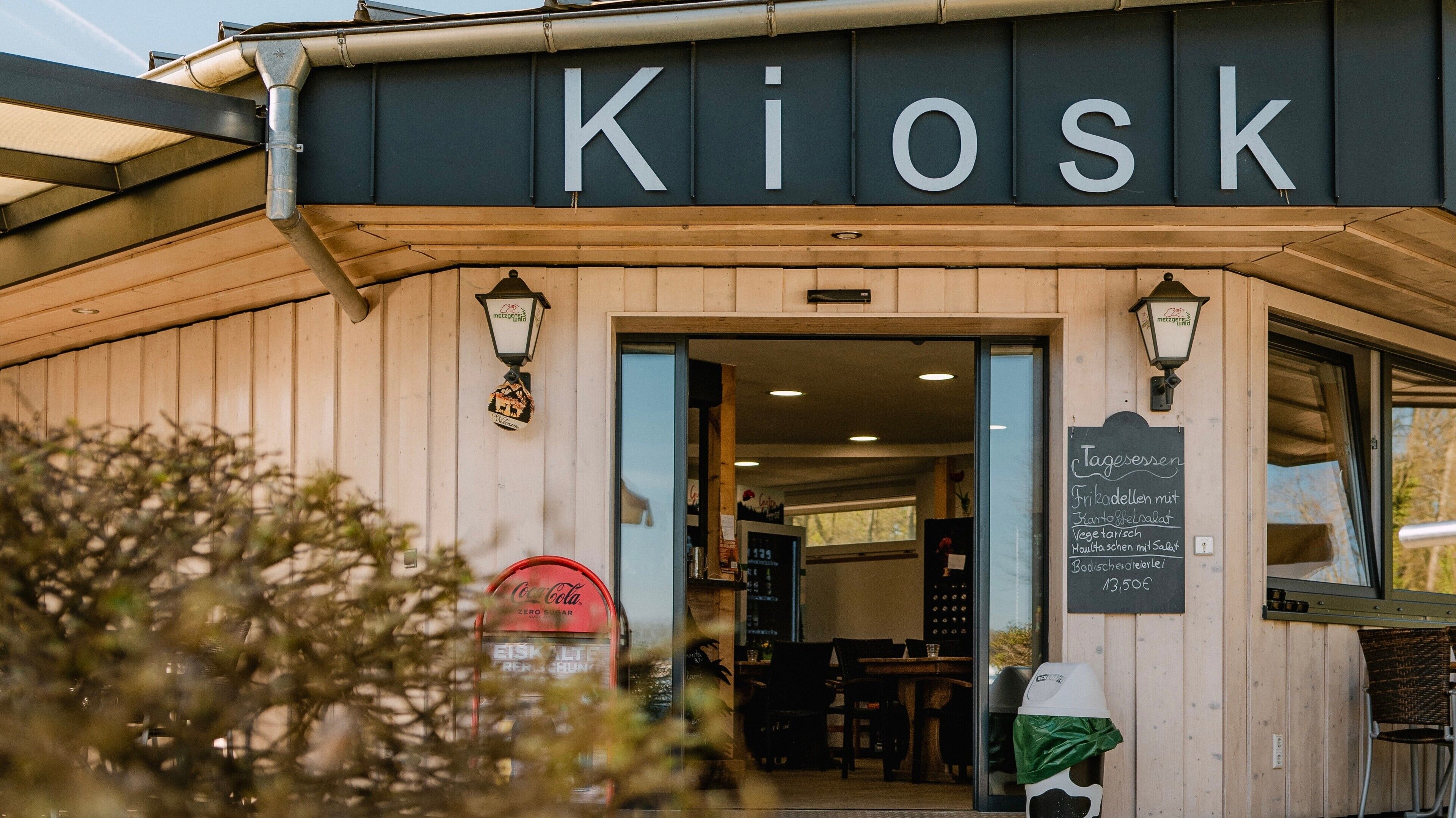 A kiosk with a sign reading 'Kiosk' and a chalkboard menu outside.